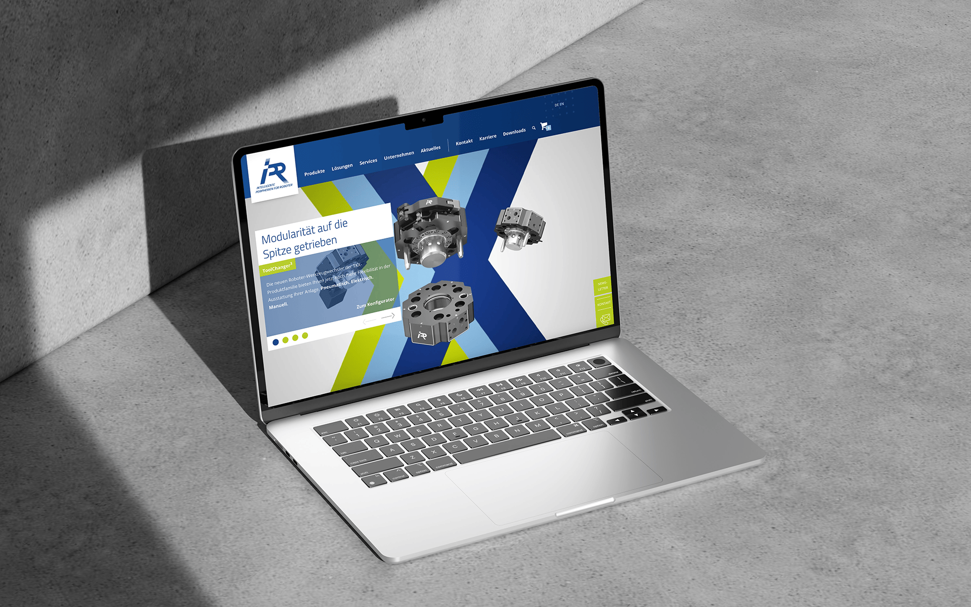 Laptop mit geöffneter IPR-Webseite auf Betonboden im Licht-Schatten-Kontrast.