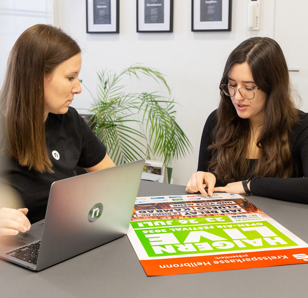 Tamara und Monique besprechen an einem Tisch das Plakat zu Haigern Live